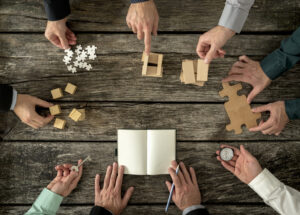 Eight businessmen planning a strategy in business advancement each holding  different but equally important metaphorical element - compass,  puzzle pieces, pegs, cubes, key and one making notes.